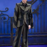 Isaac Ordonez ethnicity article image showing the young actor wearing a stylish black and olive striped suit while posing on a blue carpet event backdrop with decorative gate elements.