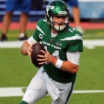 Sam Darnold injury-related image showing the NFL quarterback in a New York Jets uniform holding the football and preparing to make a pass during a game.