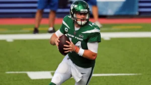 Sam Darnold injury-related image showing the NFL quarterback in a New York Jets uniform holding the football and preparing to make a pass during a game.