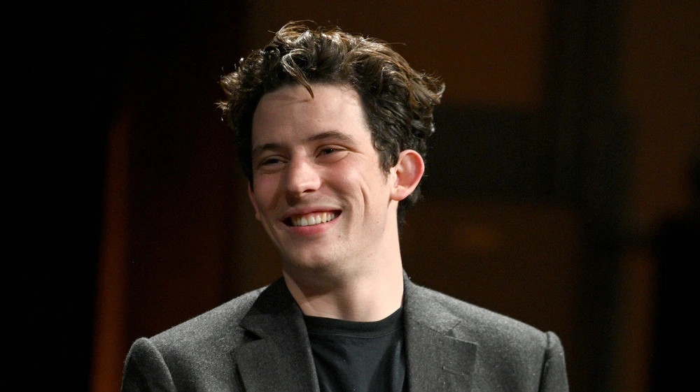 **Josh O'Connor ears visible as the actor smiles during a public appearance in a dark blazer and black shirt**